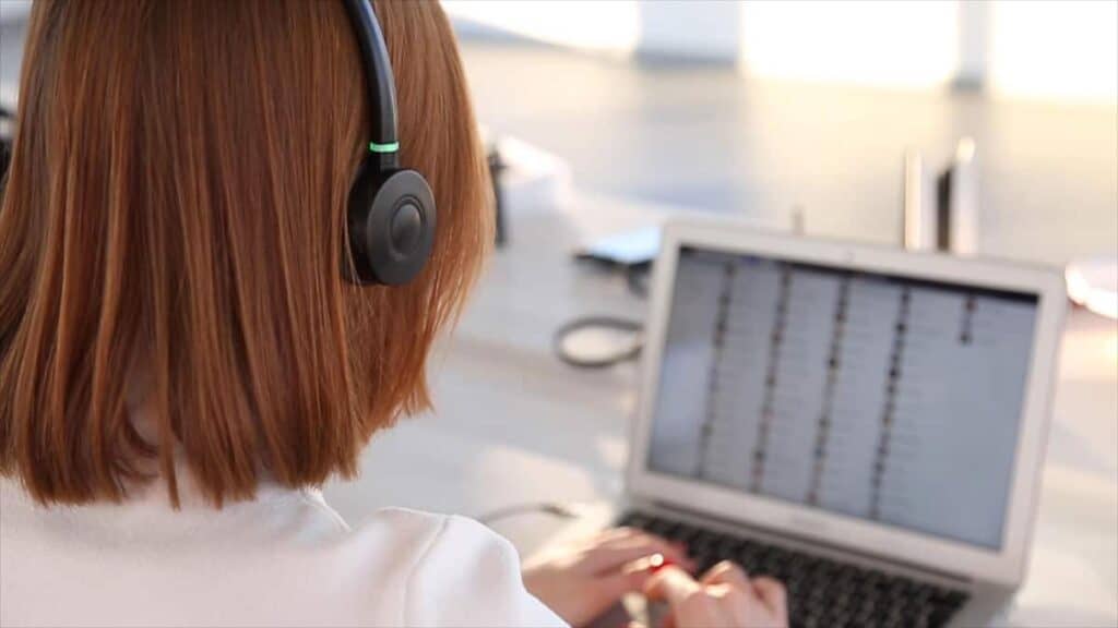 High-angle shot of a woman with headphones working on a laptop in an office setting, focusing on IT support and tech services by CNiC Solutions.