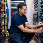Expert IT technician managing and organizing network cables and servers in a data center for optimal performance.