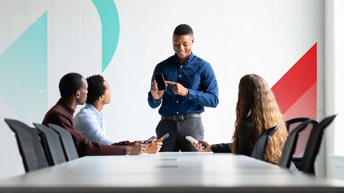 Young professional presenting mobile device to diverse team during business meeting at modern office.