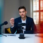 High-quality image of a professional man recording a podcast with a camera and microphone in a bright, modern office setting, representing IT and media services.