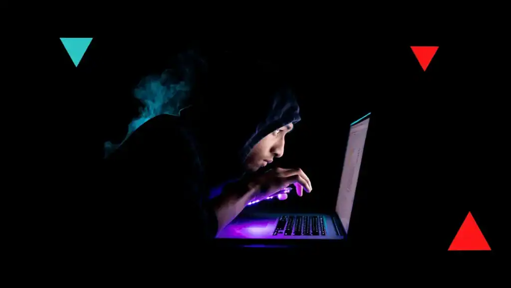 Young Hacker working on a laptop in a dark setting, emphasizing cybersecurity and IT security services.