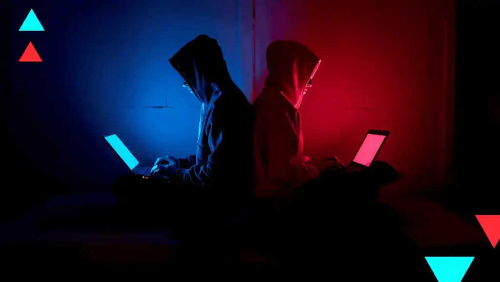 Two hackers in hoods sit back-to-back, each using a laptop in blue and red neon lighting, creating a cyber-themed scene.