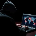 Cybersecurity threat hacker analyzing global data breach map on laptop in dark setting.