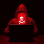 Hacker in red hoodie with skull mask working on a laptop in a dark environment, representing cybersecurity threats.