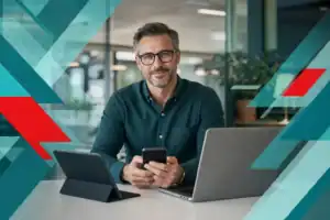 Business professional using mobile device with IT equipment in modern office setting.