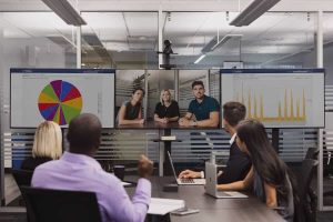 High-tech conference room with multiple monitors displaying data charts and a video call, showcasing IT solutions and collaboration technology at CNiC Solutions.